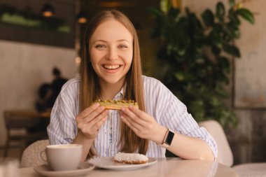 Genç sarışın kadın kafede oturmuş ekkin yiyor. Lokantada ekini kıran kız çok neşeli görünüyor. Yemek günü konseptini aldatmak. Kadın ekkin yemek için iştahla hazırlanıyor. Fıstık fırınının tadını çıkar.