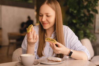 Genç sarışın kadın kafede oturmuş ekkin yiyor. Lokantada ekini kıran kız çok neşeli görünüyor. Yemek günü konseptini aldatmak. Kadın ekkin yemek için iştahla hazırlanıyor. Fıstık fırınının tadını çıkar.