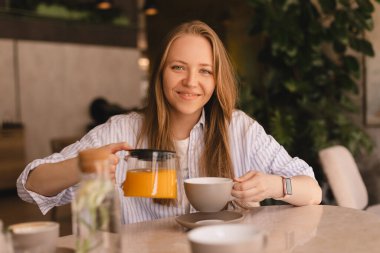 Sarışın kadın masada oturmuş, restoranda çay içiyor. Kadın kendisi ve cam çaydanlıktan arkadaşı için portakal çayı döken bir gömlek giyer ve kafede fincanlara doldurur. Mutlu kız ve arkadaşlarınla dinlen, kokunun tadını çıkar..