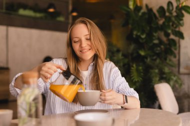 Sarışın kadın masada oturmuş, restoranda çay içiyor. Kadın kendisi ve cam çaydanlıktan arkadaşı için portakal çayı döken bir gömlek giyer ve kafede fincanlara doldurur. Mutlu kız ve arkadaşlarınla dinlen, kokunun tadını çıkar..