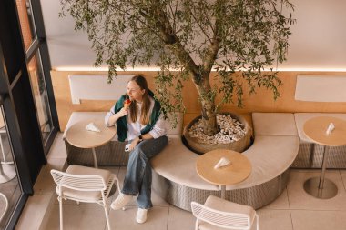 Kadın turist, açık hava restoranında otururken dondurma yiyor. Şehirde yaz tatilinin tadını çıkaran mutlu sarışın kadın. Kafede oturan ve waffle külahında pembe dondurmayı yalayan kız..