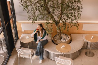 Kadın turist, açık hava restoranında otururken dondurma yiyor. Şehirde yaz tatilinin tadını çıkaran mutlu sarışın kadın. Kafede oturan ve waffle külahında pembe dondurmayı yalayan kız..
