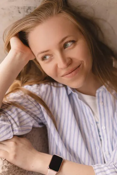 Evdeki portre için poz veren sarışın kadın portresi, rahat koltukta oturuyor, gülümsüyor, gülüyor, başını yana yaslıyor. Şehvetli görün ve rüya gör. Gömleğini giy.