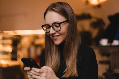 Güzel gülüşü olan, kafede dinlenirken cep telefonundan iyi haberler okuyan, Kafkasyalı mutlu bir kadın, boş zamanlarında cep telefonundan resimlerini seyrediyor..