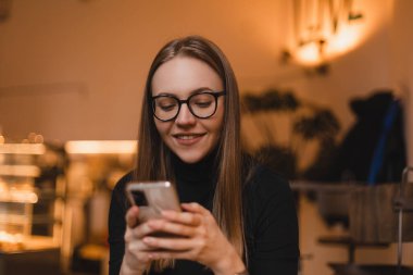 Güzel gülüşü olan, kafede dinlenirken cep telefonundan iyi haberler okuyan, Kafkasyalı mutlu bir kadın, boş zamanlarında cep telefonundan resimlerini seyrediyor..