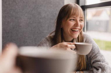 Kafede çay içerken gülümseyen ve konuşan beyaz kadınlar. Kızlar iyi sohbet eder, dedikodu yapar, güler. İnsanlar, iletişim ve arkadaşlık kavramı - çay içen gülümseyen genç kadınlar.