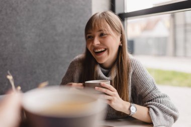 Kafede çay içerken gülümseyen ve konuşan beyaz kadınlar. Kızlar iyi sohbet eder, dedikodu yapar, güler. İnsanlar, iletişim ve arkadaşlık kavramı - çay içen gülümseyen genç kadınlar.