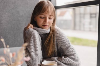 Kafedeki ya da restorandaki kanepede oturan mutlu genç kadın. Koltuğunda rahat bir kadın portresi. Gülümseyen ve rahatlatan güzel bir kızın portresi. Masada bir fincan sıcak çay..