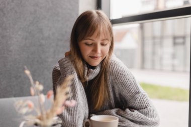 Kafedeki ya da restorandaki kanepede oturan mutlu genç kadın. Koltuğunda rahat bir kadın portresi. Gülümseyen ve rahatlatan güzel bir kızın portresi. Masada bir fincan sıcak çay..