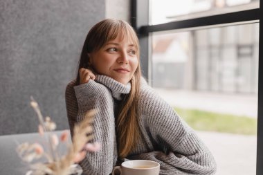 Kafedeki ya da restorandaki kanepede oturan mutlu genç kadın. Koltuğunda rahat bir kadın portresi. Gülümseyen ve rahatlatan güzel bir kızın portresi. Masada bir fincan sıcak çay..