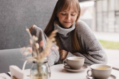 Kafedeki ya da restorandaki kanepede oturan mutlu genç kadın. Koltuğunda rahat bir kadın portresi. Gülümseyen ve rahatlatan güzel bir kızın portresi. Masada bir fincan sıcak çay..