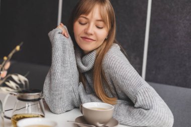 Kafedeki ya da restorandaki kanepede oturan mutlu genç kadın. Koltuğunda rahat bir kadın portresi. Gülümseyen ve rahatlatan güzel bir kızın portresi. Masada bir fincan sıcak çay..