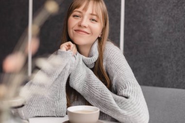 Kafedeki ya da restorandaki kanepede oturan mutlu genç kadın. Koltuğunda rahat bir kadın portresi. Gülümseyen ve rahatlatan güzel bir kızın portresi. Masada bir fincan sıcak çay..