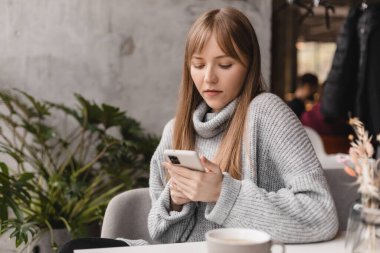 Seks düşkünü genç sarışın kadın kafeteryada oturuyor akıllı telefon, mesajlar, telefon görüşmeleri, mektuplar, mesajlar, mesajlar, yazışmalar, sohbet ya da mesajlar okuyor. Kız mesajlaşması, telefonla ödeme..