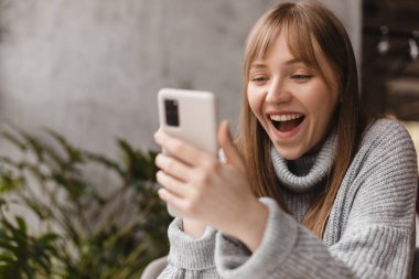 Cep telefonunda video oyunu oynayan neşeli sarışın kadın, iyi haberler okuyor, piyangoyu kazanmayı kutluyor, kazanan hareketi yaparken çok mutlu ve neşeli hissediyor. Vay canına..