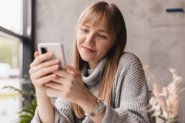 Seks düşkünü genç sarışın kadın kafeteryada oturuyor akıllı telefon, mesajlar, telefon görüşmeleri, mektuplar, mesajlar, mesajlar, yazışmalar, sohbet ya da mesajlar okuyor. Kız mesajlaşması, telefonla ödeme..