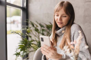 Seks düşkünü genç sarışın kadın kafeteryada oturuyor akıllı telefon, mesajlar, telefon görüşmeleri, mektuplar, mesajlar, mesajlar, yazışmalar, sohbet ya da mesajlar okuyor. Kız mesajlaşması, telefonla ödeme..