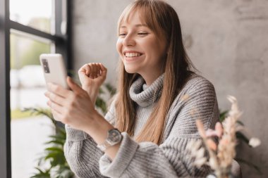 Cep telefonunda video oyunu oynayan neşeli sarışın kadın, iyi haberler okuyor, piyangoyu kazanmayı kutluyor, kazanan hareketi yaparken çok mutlu ve neşeli hissediyor. Vay canına..