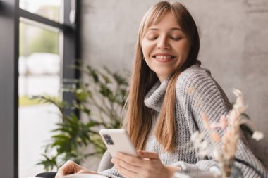 Seks düşkünü genç sarışın kadın kafeteryada oturuyor akıllı telefon, mesajlar, telefon görüşmeleri, mektuplar, mesajlar, mesajlar, yazışmalar, sohbet ya da mesajlar okuyor. Kız mesajlaşması, telefonla ödeme..