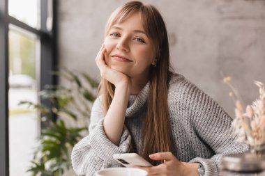 Seks düşkünü genç sarışın kadın kafeteryada oturuyor akıllı telefon, mesajlar, telefon görüşmeleri, mektuplar, mesajlar, mesajlar, yazışmalar, sohbet ya da mesajlar okuyor. Kız mesajlaşması, telefonla ödeme..