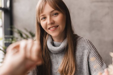 Erkek avucunun içinde kadın avucu. Romantik randevu konsepti. El ele tutuşurken kahve içen bir çift. Kadın gülüyor, sevgilisine bak. Gri kazak giy, mutlu görün, gülümse..