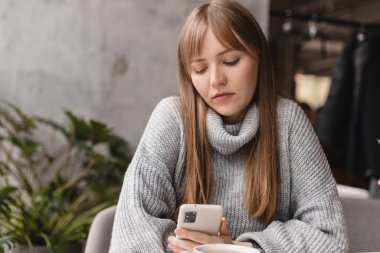 Seks düşkünü genç sarışın kadın kafeteryada oturuyor akıllı telefon, mesajlar, telefon görüşmeleri, mektuplar, mesajlar, mesajlar, yazışmalar, sohbet ya da mesajlar okuyor. Kız mesajlaşması, telefonla ödeme..