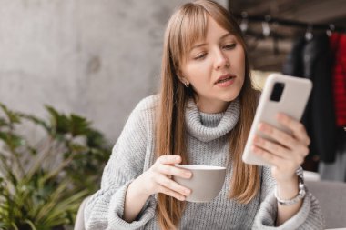 Seks düşkünü genç sarışın kadın kafeteryada oturuyor akıllı telefon, mesajlar, telefon görüşmeleri, mektuplar, mesajlar, mesajlar, yazışmalar, sohbet ya da mesajlar okuyor. Kız mesajlaşması, telefonla ödeme..