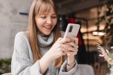 Seks düşkünü genç sarışın kadın kafeteryada oturuyor akıllı telefon, mesajlar, telefon görüşmeleri, mektuplar, mesajlar, mesajlar, yazışmalar, sohbet ya da mesajlar okuyor. Kız mesajlaşması, telefonla ödeme..