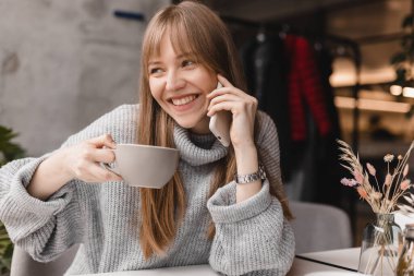 Sarışın kadın, olumlu bir şekilde gülümsüyor ve arkadaşıyla telefonda konuşuyor. Sıcak bir çay içiyor. Keyifli bir hafta sonu tatili geçiriyor. Kız tartıştı..