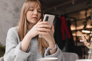 Seks düşkünü genç sarışın kadın kafeteryada oturuyor akıllı telefon, mesajlar, telefon görüşmeleri, mektuplar, mesajlar, mesajlar, yazışmalar, sohbet ya da mesajlar okuyor. Kız mesajlaşması, telefonla ödeme..