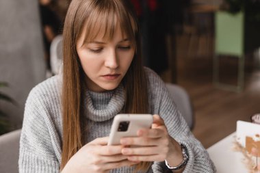 Seks düşkünü genç sarışın kadın kafeteryada oturuyor akıllı telefon, mesajlar, telefon görüşmeleri, mektuplar, mesajlar, mesajlar, yazışmalar, sohbet ya da mesajlar okuyor. Kız mesajlaşması, telefonla ödeme..