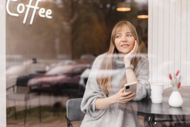 Seks düşkünü genç sarışın kadın kafeteryada oturuyor akıllı telefonları tutuyor, mesajları cevaplıyor, telefon görüşmeleri, mektuplar, pencerenin altına fotoğraf koyuyor. Kız mesajlaşması, telefonla ödeme..