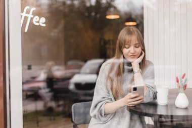 Seks düşkünü genç sarışın kadın kafeteryada oturuyor akıllı telefonları tutuyor, mesajları cevaplıyor, telefon görüşmeleri, mektuplar, pencerenin altına fotoğraf koyuyor. Kız mesajlaşması, telefonla ödeme..