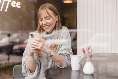 Seks düşkünü genç sarışın kadın kafeteryada oturuyor akıllı telefonları tutuyor, mesajları cevaplıyor, telefon görüşmeleri, mektuplar, pencerenin altına fotoğraf koyuyor. Kız mesajlaşması, telefonla ödeme..