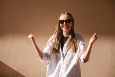 Neşeli, güzel bir kadın kutlama yapıyor, inançsızlık ve heyecanla ödül kazanıyor, şampiyon gibi tezahürat yapıyor, iyi haberlerden bağırıyor ve zafer kazanıyor, dışarıda bej duvarın yanında duruyor..