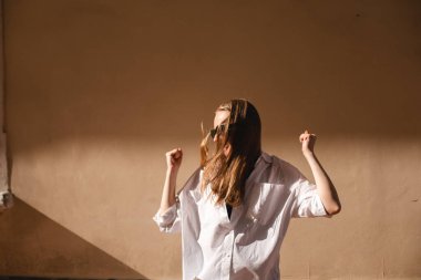 Neşeli, güzel bir kadın kutlama yapıyor, inançsızlık ve heyecanla ödül kazanıyor, şampiyon gibi tezahürat yapıyor, iyi haberlerden bağırıyor ve zafer kazanıyor, dışarıda bej duvarın yanında duruyor..