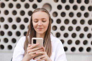 Şehirdeki mutlu sarışın kadın sosyal ağda cep telefonu sohbeti yapıyor. Aktif şehir gençliği kavramı. Kız cep telefonunu tut ve sohbet et, mesajlaş, mutlu görün..