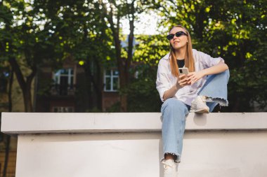 İnsanların duyguları, yaşam tarzı, eğlence ve güzellik konsepti. Hayalci ve heyecanlı genç sarışın kadın cep telefonu kullanıyor, gülümsüyor ve düşünceli görünüyor, bir fikri var, çözümler arıyor, düşünüyor..