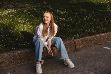 Kendine güvenen güzel bir kadının portresi doğada gülümsüyor, parkta yürüyor ve yan yana bakıyor. Mutlu sarışın kadın yan yana bak, doğanın tadını çıkar, beyaz gömlekli ve kot pantolonlu kadın şaşırt..