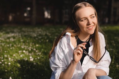 Güzel, açık havada, sarı saçlı, zarif bluzlu, beyaz gömlekli, çiçekli, güzel, seksi bir kadın fotoğrafı. Kadın bardakları ısırır ve hayal görür.