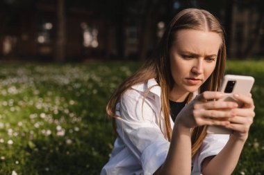 Elini çenesinde tutarken telefonu tutan bir kadın. Kampüs dışında düşünen etkileyici bir öğrenci, elinde akıllı telefon olan kuşkulu bir kadın bilgi okumayı, arama çözümü bulmayı düşünüyor..