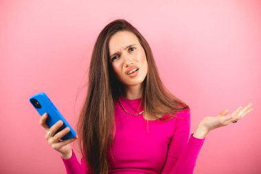 Pembe arka planda izole edilmiş cep telefonu kullanan genç ve güzel bir kadın. Bağıran mutsuz kadın cep telefonunu tutuyor. Hayal kırıklığına uğramış üzgün bayan, haberleri dehşete düşürdü. Bu da ne? Olamaz..