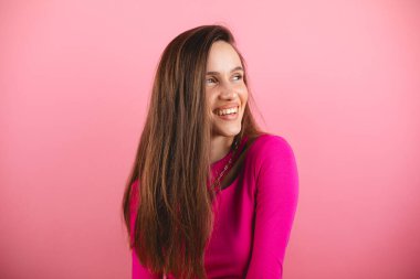 Pembe uzun kollu mutlu genç kadın pozitif haber ya da doğum günü hediyesine sevinerek sevinçli ve büyüleyici bir gülümsemeyle kameraya bakıyor. Esmer kız izole pembeyi gevşetiyor. Yana bak..