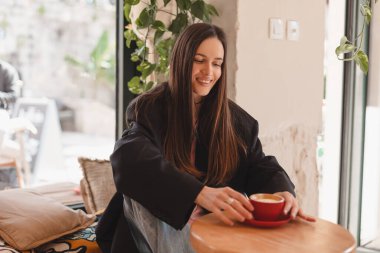 Kafede kahve içen düşünceli esmer kadın, yaşam tarzı, kahve, iletişim ve yerel iş, değişmemiş. Mutlu kız cappuccino içer, kafeteryada dinlenir.