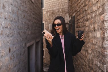 Mutlu gülümseyen esmer kadın heyecanlı yüz ifadesiyle akıllı telefonu tutuyor, oynadığına, piyangoyu kazandığına, iyi haberler okuduğuna inanamıyor, falına inanamıyor. Kucaklaşmaya hazır ol..