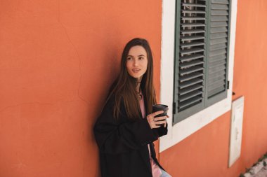 Turuncu duvarın yanında duran şehvetli kadın eski şehirde yürüyor, kahve ya da çayla götürmek için fincanı tutuyor. Kadınlar sokakta dinlenirken cappuccino içer..