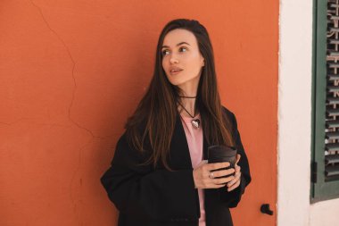 Turuncu duvarın yanında duran şehvetli kadın eski şehirde yürüyor, kahve ya da çayla götürmek için fincanı tutuyor. Kadınlar sokakta dinlenirken cappuccino içer..