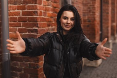 Güzel esmer kadın siyah kabarık bir ceket giyiyor kameraya bakıyor sarılmak için gülümsüyor, neşeli bir ifade mutluluğu kucaklıyor, arkadaşlarıyla ya da aileleriyle mutlu bir şekilde buluşuyor..