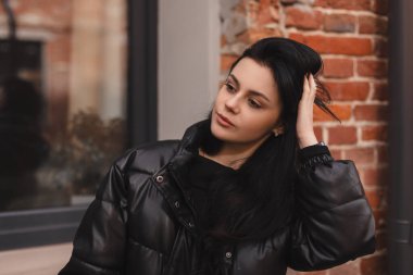 Esmer saçlı modacı kız dışarıda poz veriyor. Deri ceketli kadın saçını düzeltiyor, sokakta yürüyor. Şehirde poz veren mutlu turist kadın. İyimser bayan dışarı çıkıyor..