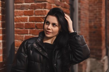 Esmer saçlı modacı kız dışarıda poz veriyor. Deri ceketli kadın saçını düzeltiyor, sokakta yürüyor. Şehirde poz veren mutlu turist kadın. İyimser bayan dışarı çıkıyor..